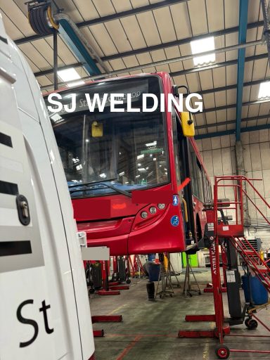 Supporting Londons Buses Red bus in a workshop, elevated on a lift with tools and equipment around.