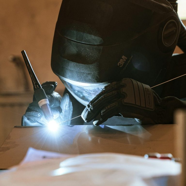 A welder working with a torch, wearing safety gear and focused on their task.