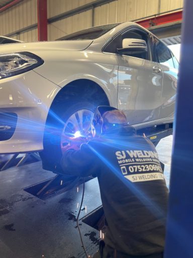A mechanic repairs a vehicle's wheel in a garage, using a tool with bright sparks.