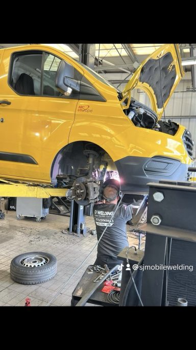 Engine timing cover welding repairs A mechanic working on the engine of a yellow van in a garage.